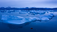 In this Aug. 15, 2019, photo, a boat navigates at night next to large icebergs near the town of Kulusuk, in eastern Greenland. 